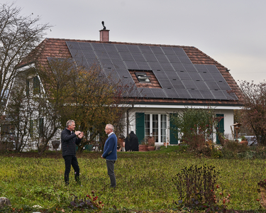 Einfamiilenhaus mit motnierter PV-Anlage auf der ganzen Dachbreite, vor dem Haus sind zwei Herren im Gespräch