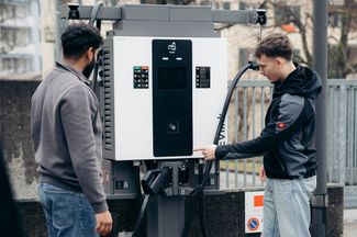 Zwei Männer bezahlen den Ladevorgang an einer öffentlichen Ladestation für Elektroautos.