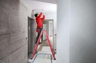 Elektroinstallateur auf einer Leiter bei Arbeit