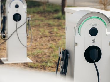 Ein weisses Elektroauto lädt an einer Ladestation im Aussenbereich eines Unternehmens. Daneben sind weitere Ladestationen zu sehen.