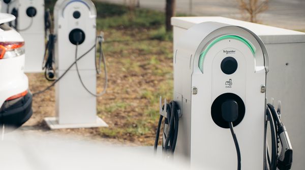 Ein weisses Elektroauto lädt an einer Ladestation im Aussenbereich eines Unternehmens. Daneben sind weitere Ladestationen zu sehen.