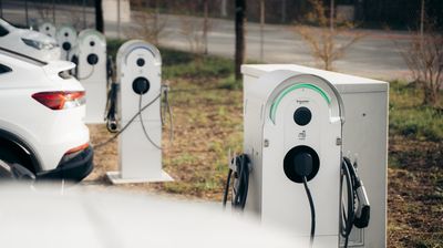Ein weisses Elektroauto lädt an einer Ladestation im Aussenbereich eines Unternehmens. Daneben sind weitere Ladestationen zu sehen.